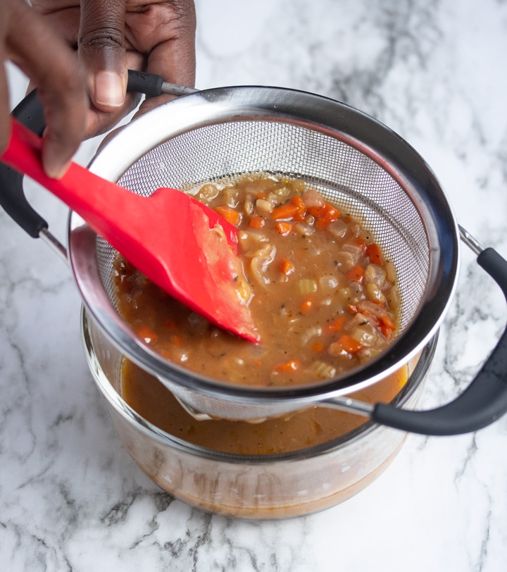 Gravy being drained through strainer with red spatula pushing it through