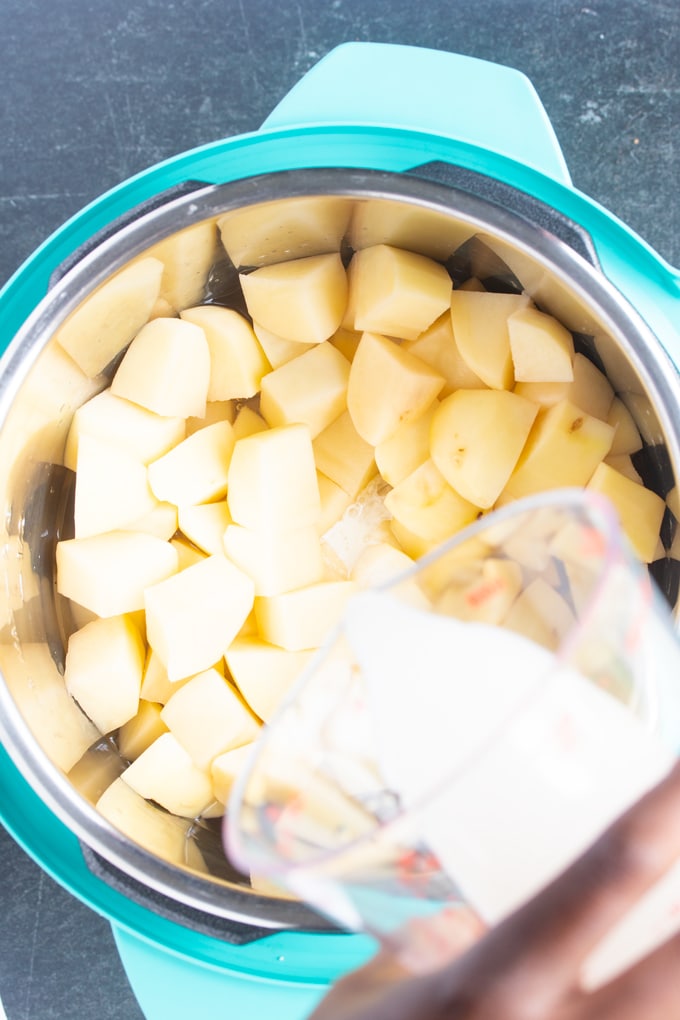 cut potatoes in instant pot insert with heavy cream being poured into the instant pot insert