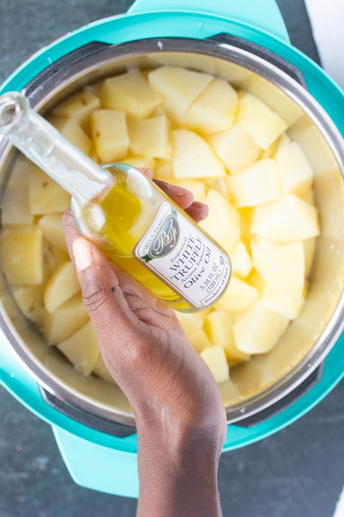 cooked mashed potatoes in instant pot insert with hand holding white truffle olive oil