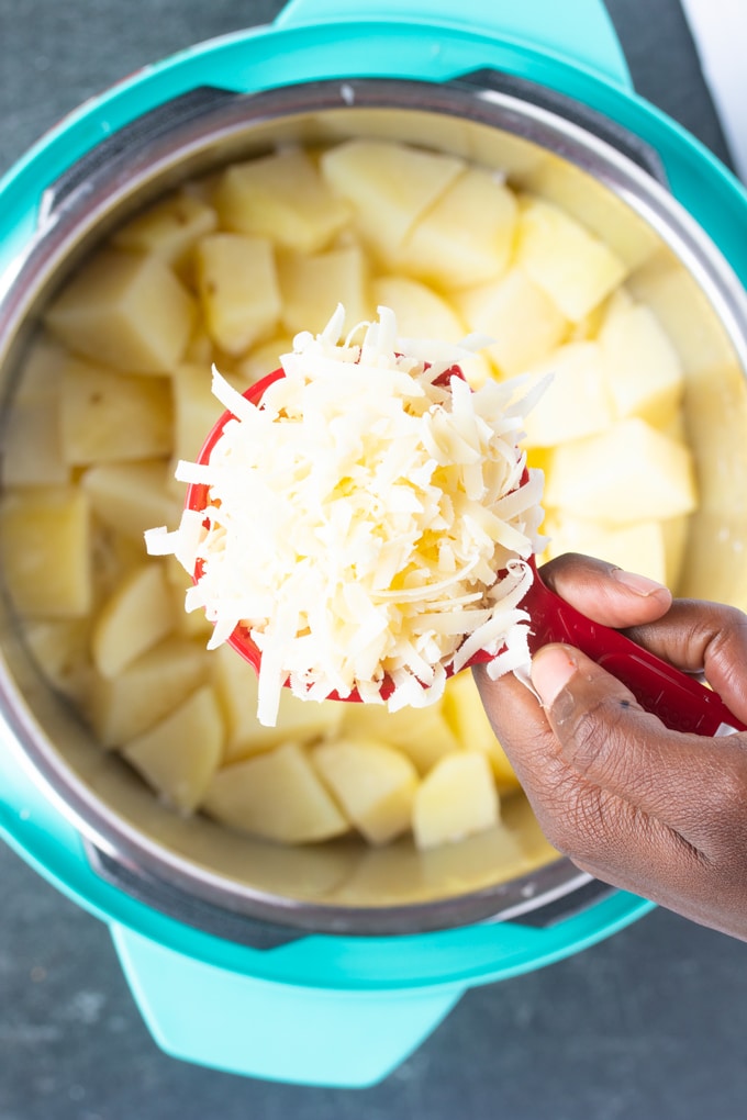 cooked mashed potatoes in instant pot insert with hand holding parmesan cheese