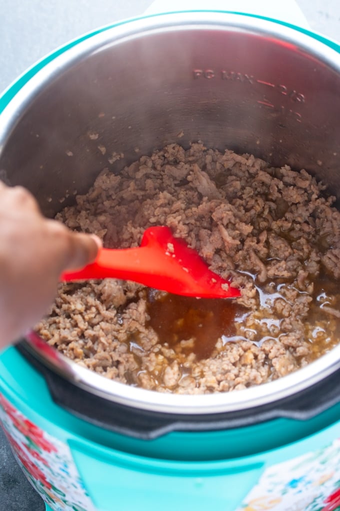 red spatula in instant pot stirring italian sausage and beef broth