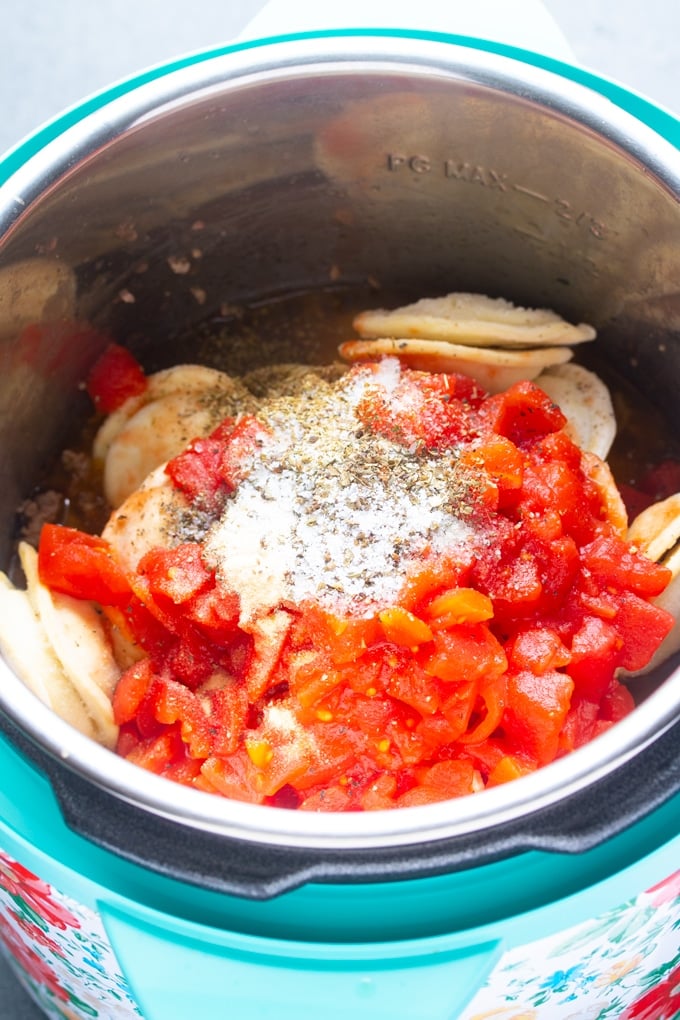 ingredients with ravioli, tomatoes, and seasoning in layers inside the instant pot