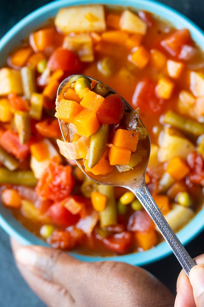 spoon holding vegetable soup over bowl with vegetable soup