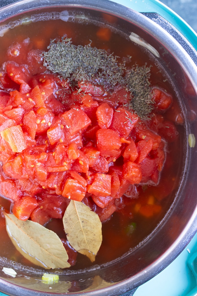 tomatoes in instant pot with basil and thyme on top.