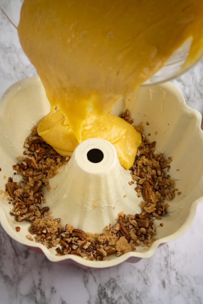 cake batter being poured into bundt pan over pecans