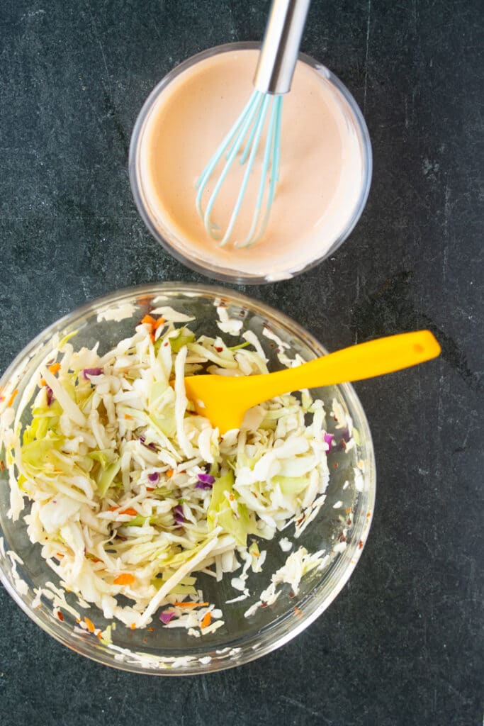 spicy mayonnaise in bowl with whisk sticking out, colesalw in bowl with yellow spatula sticking out