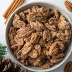 candied pecans in a bowl with cinnamon stick and pinecone around it