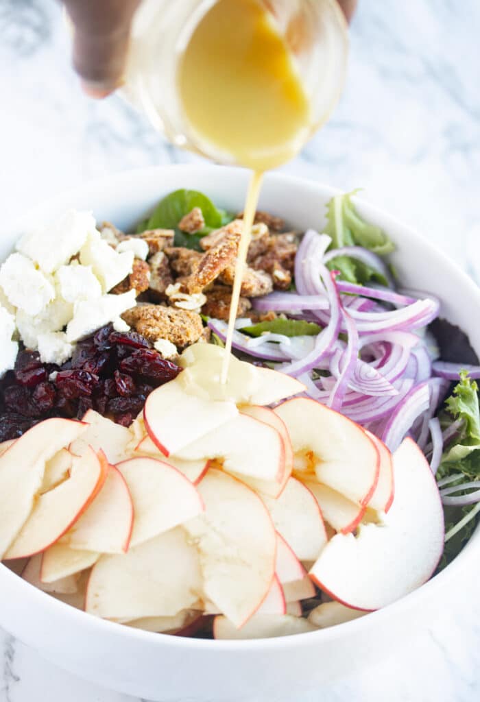 ingredients of cranberry apple salad in bowl with yellow salad dressing being poured onto salad