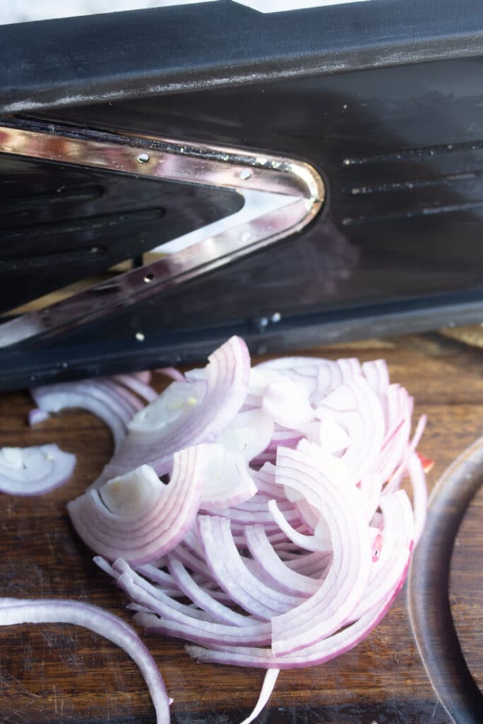 red onion thinly sliced in front of a mandolin blade