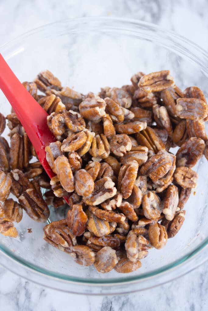 pecans covered in egg whites in bowl with red spatula sticking out