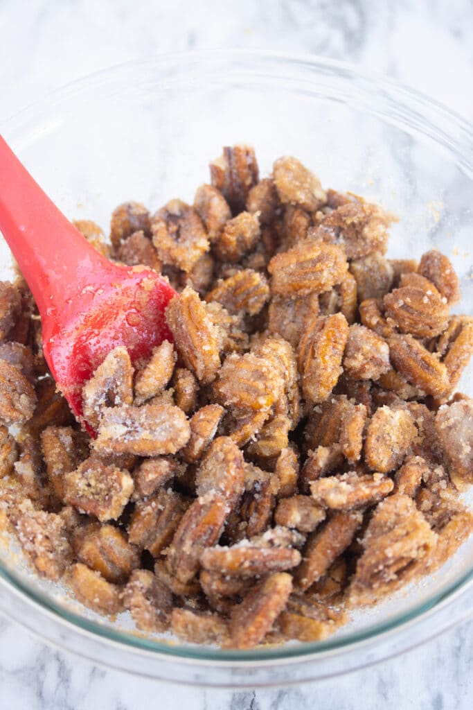 sugar on pecans in bowl with red spatula sticking out