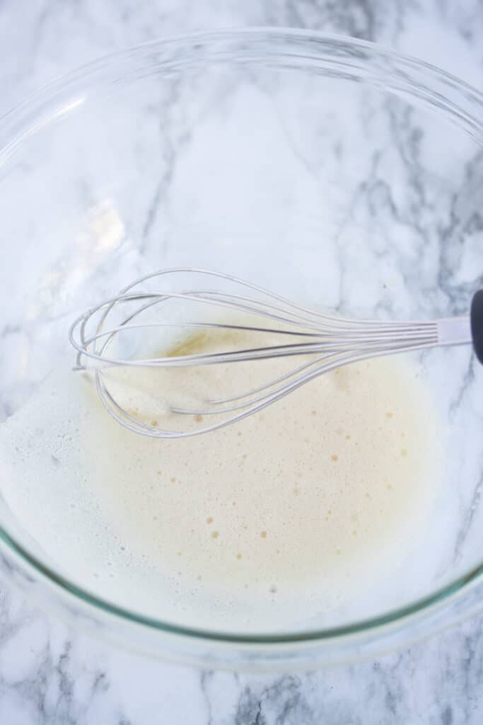 egg whites in bowl with whisk sticking out. egg whites are frothy