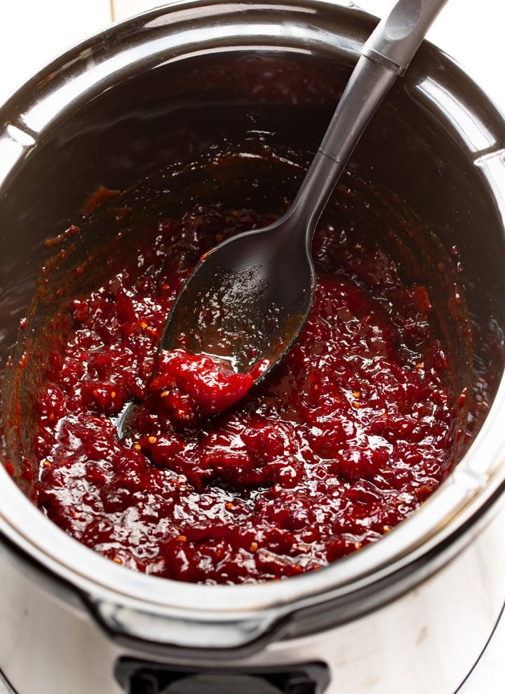 sauce for meatballs in slow cooker insert with black spoon sticking out