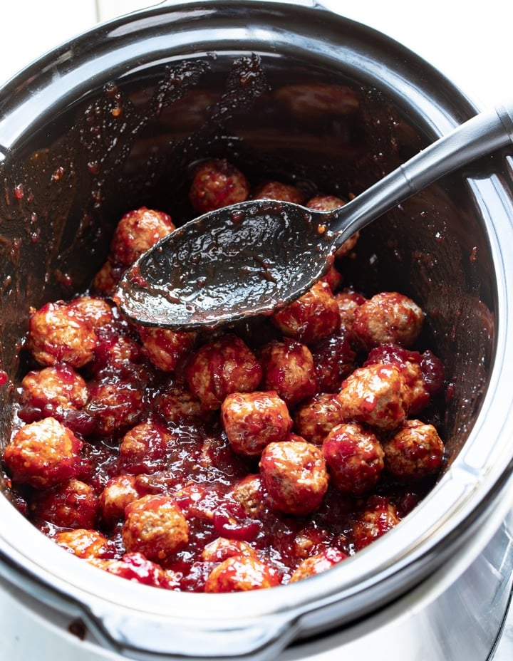 frozen meatballs covered in sauce in slow cooker insert with black spoon laying on top of meatballs