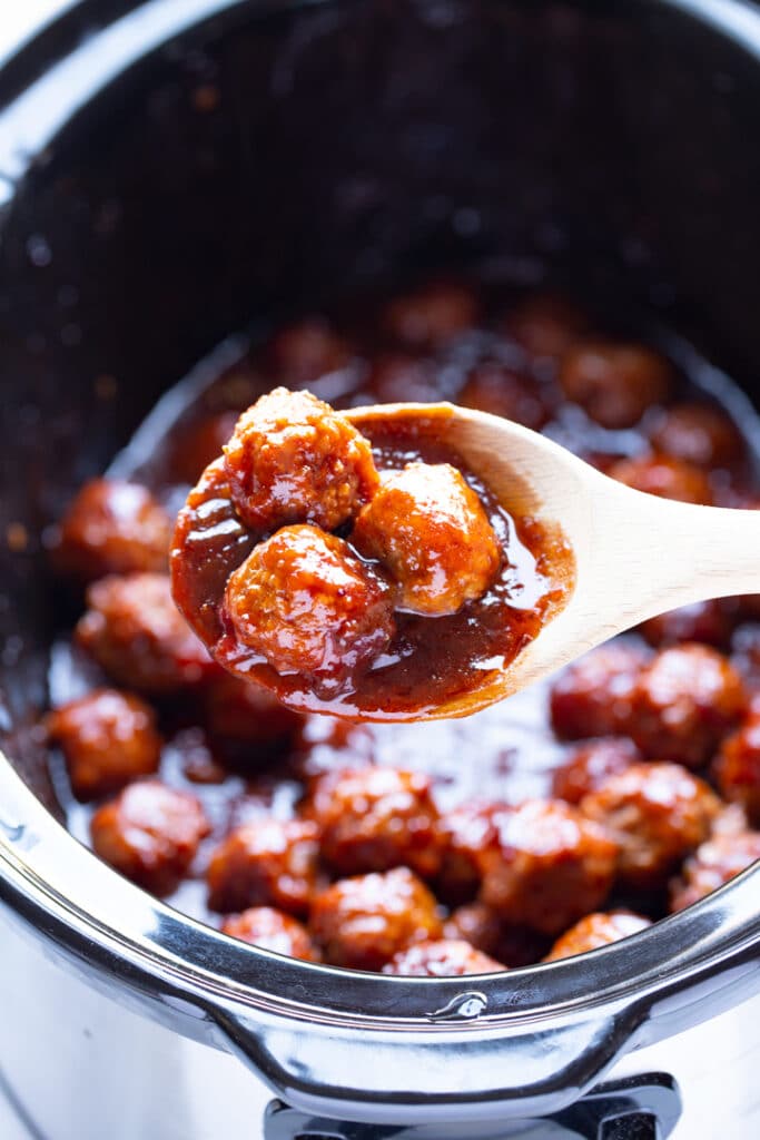 meatballs on wooden spoon over slow cooker with remainder of party meatballs