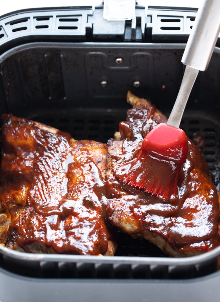 ribs in air fryer basket with sauce being brushed on it