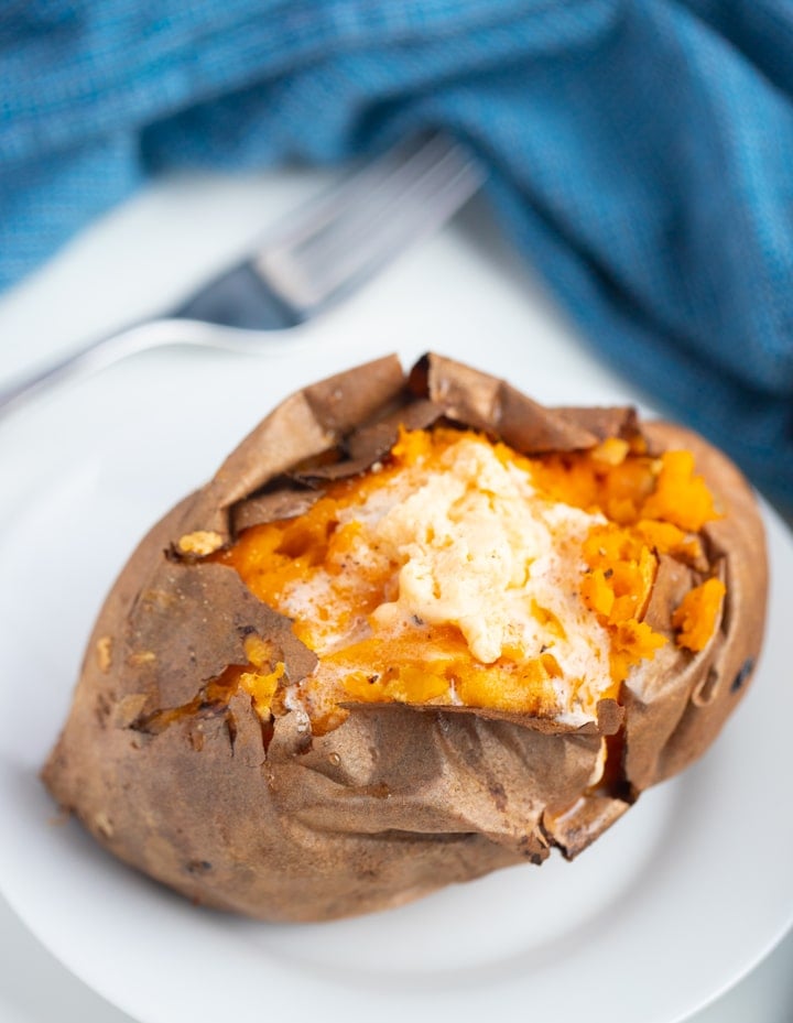 sweet potato topped with butter with fork and blue napkin in the background