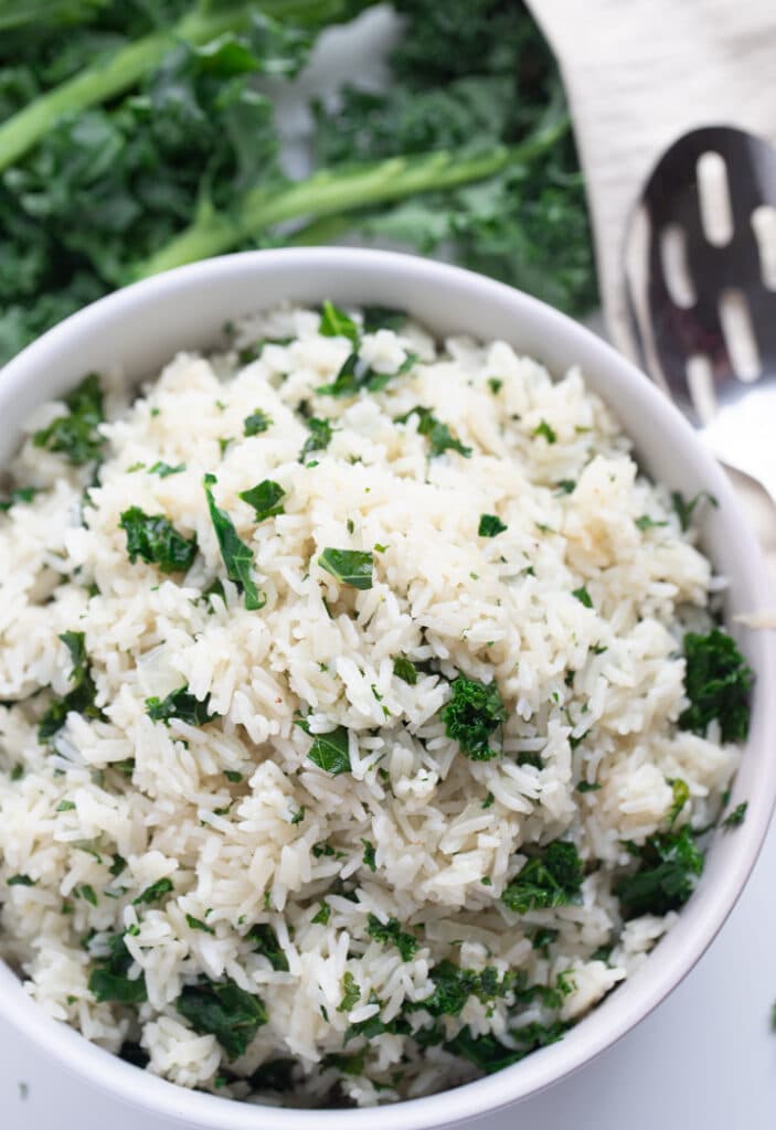 kale rice in white bowl with spoon and kale in background