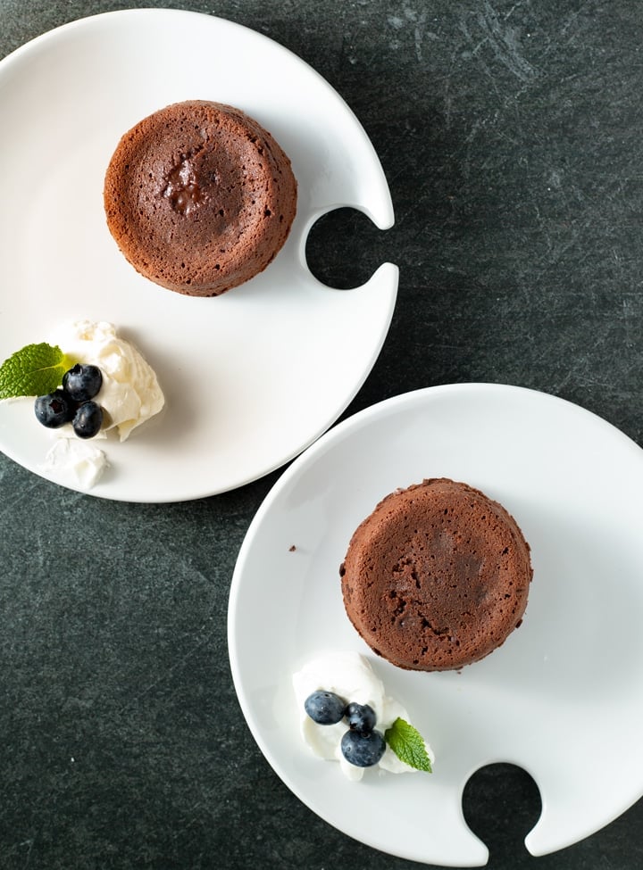 molten lava cakes on little white plates with whipped cream and blueberries and mint on plate