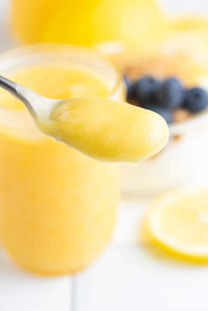 lemon curd on spoon in front of lemon curd in jars