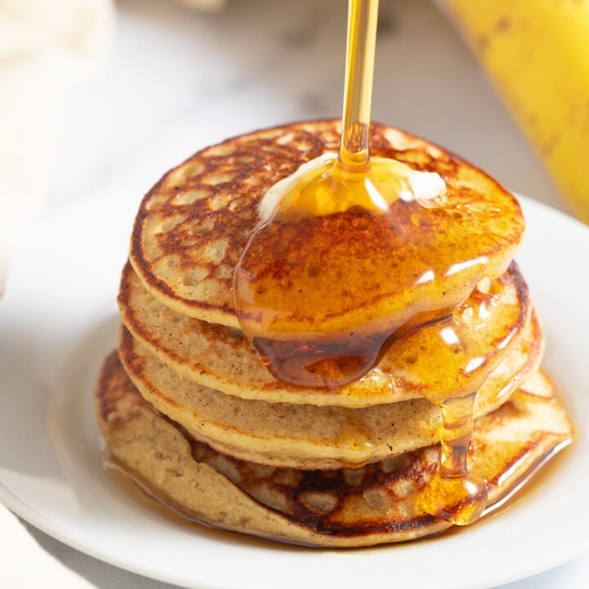 banana oatmeal pancakes with syrup being poured on top