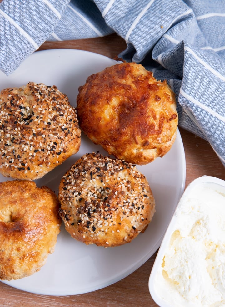 bagels on a plate with blue towel around them next to a tub of cream cheese
