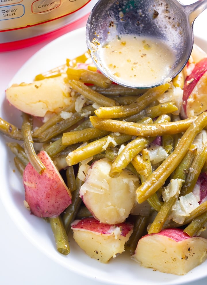 Sauce being poured over a dish of green beans and potatoes