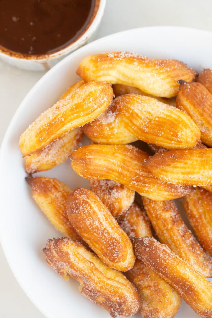 Churros in a white bowl next to chocolate dipping sauce