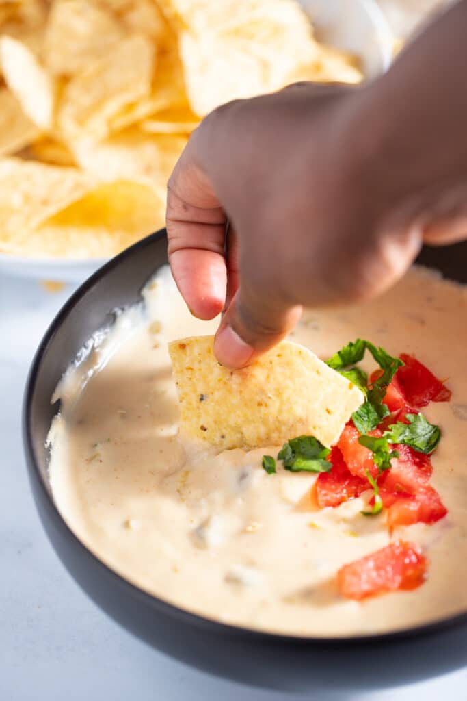 A tortilla being dipped into the queso dip 