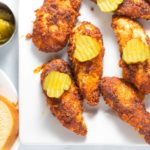 finished hot chicken tenders in a plate with pickles on top
