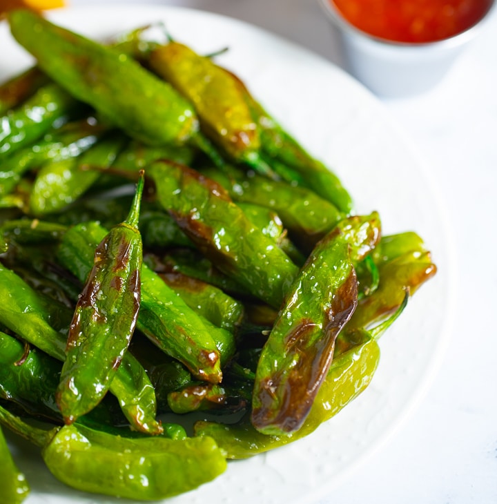 Close up of roasted shishito peppers in a white bowl