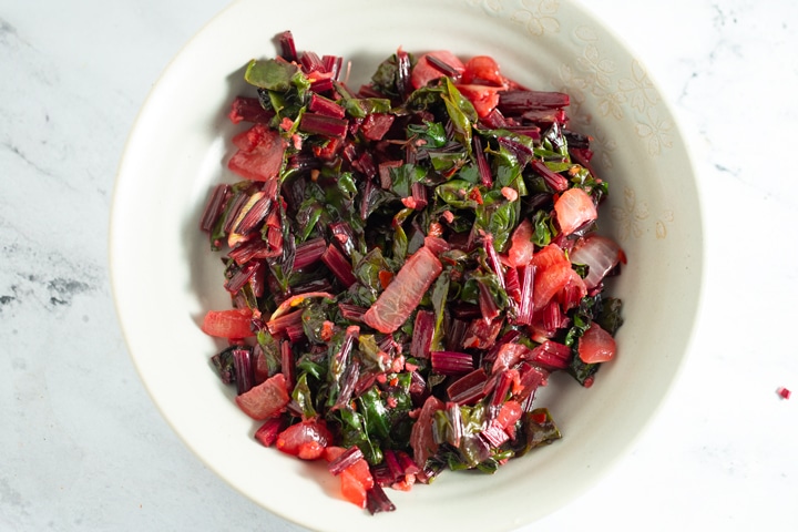 Beet greens in a white bowl on a marble work surface