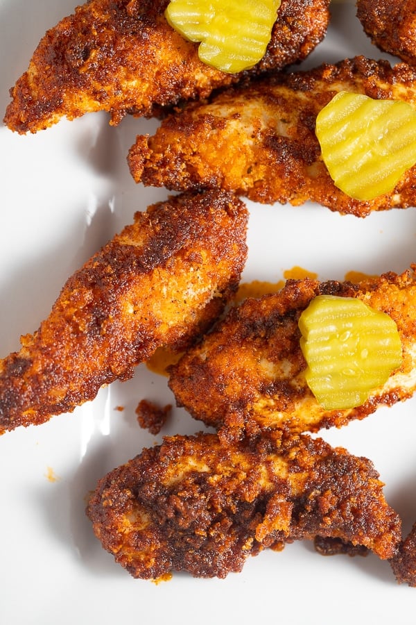 hot chicken tenders on white plate with pickles on top