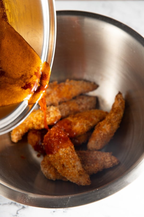 Sauce being poured over the chicken tenders