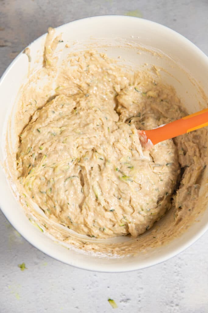 Mixing the zucchini muffin batter in a white bowl