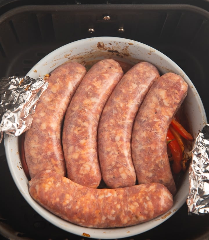 Uncooked sausages laid on top of the cooked vegetables