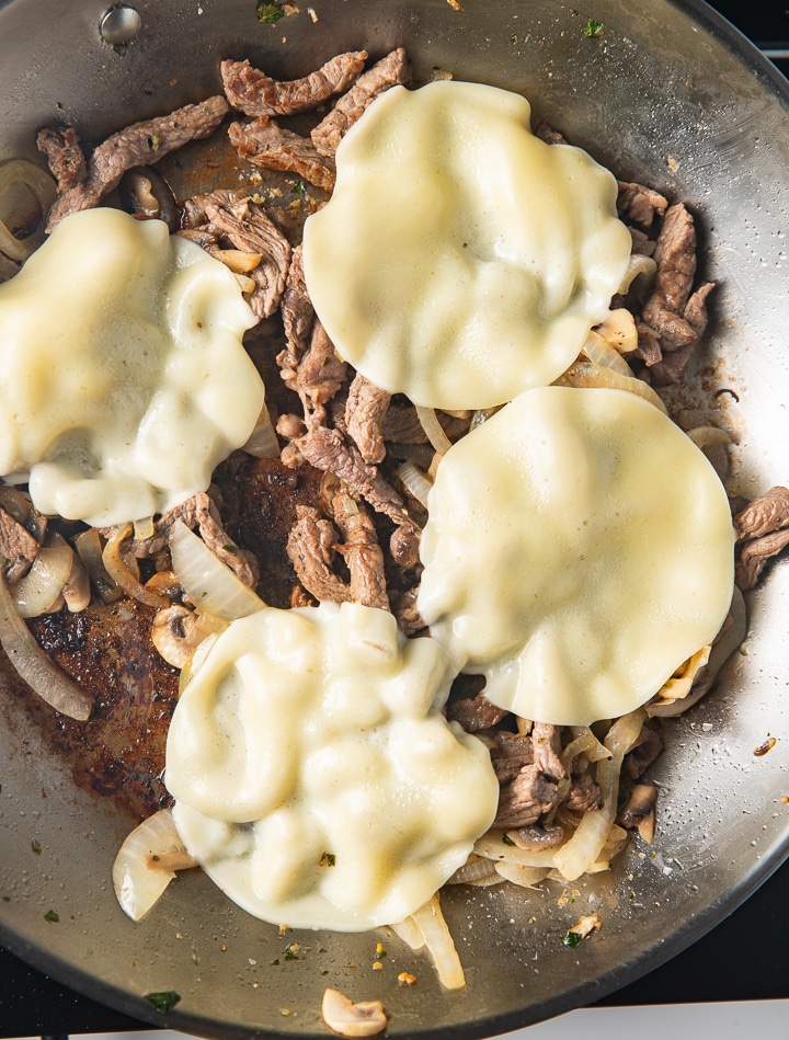 Cheese added to the top of the steak in a pan