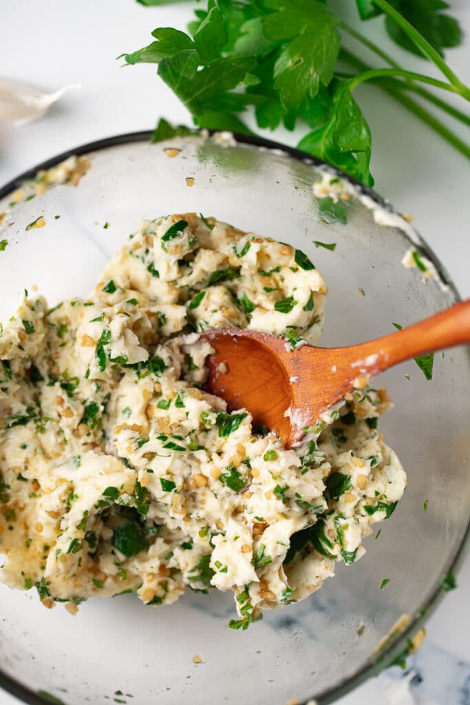 Garlic herb butter in a glass bowl with a wooden spoon