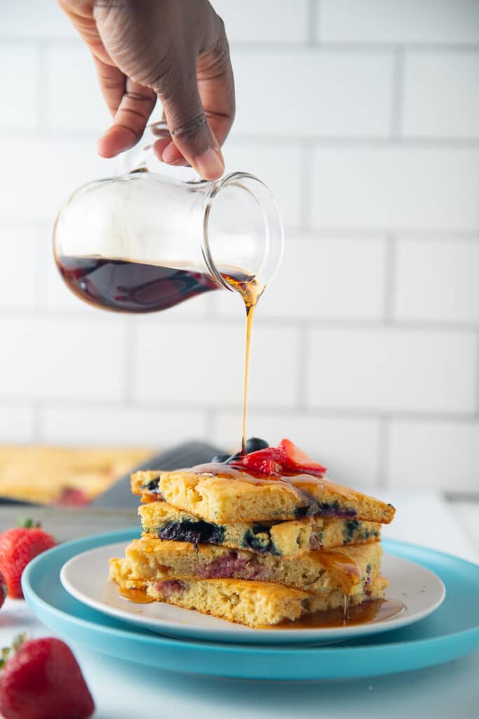 A hand pouring syrup over sheet pan pancakes