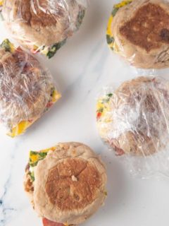 breakfast sandwiches wrapped in plastic wrap on marble with one sandwich unwrapped