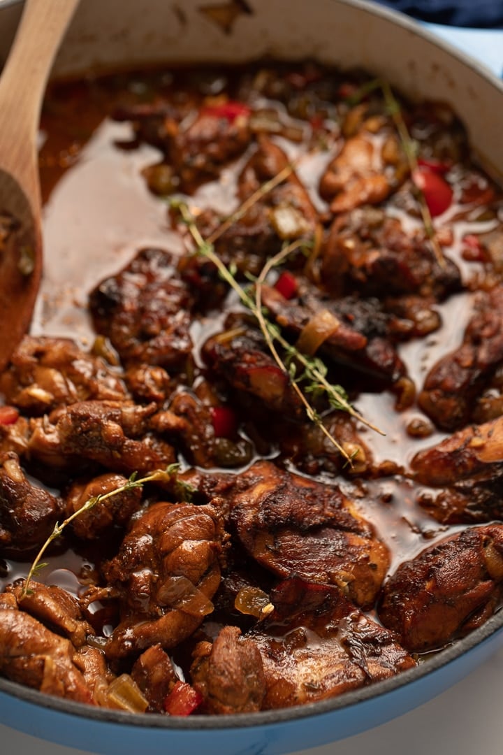 close up photo of brown stew chicken in pan with thyme leaves on top