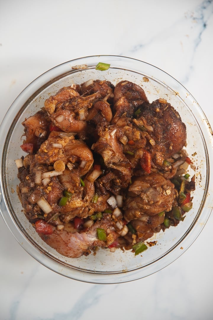 raw chicken with peppers, onions, and other seasonings in glass bowl