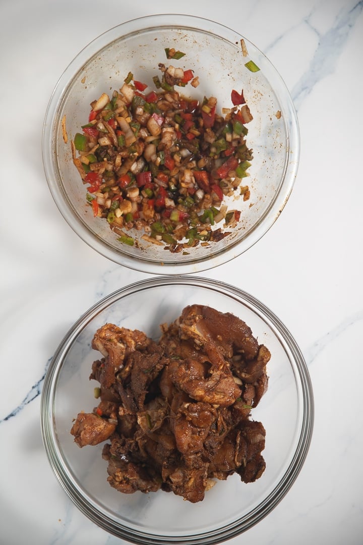 two glass bowls, one with peppers and onions and the other with raw chicken