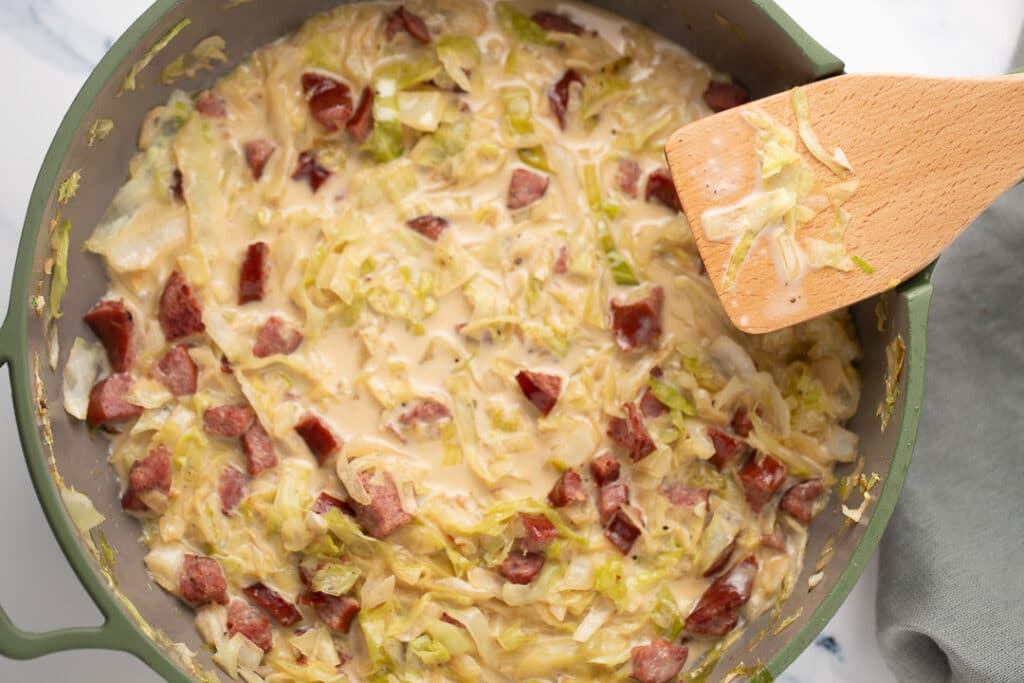 Overhead shot of creamed cabbage and sausage in a skillet with a wooden spatula