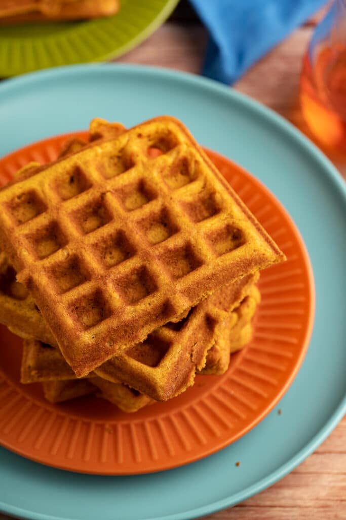 pumpkin waffles stacked on top of each other on orange and teal plate