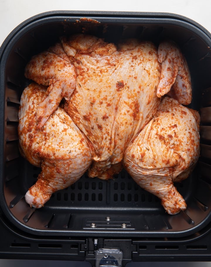The seasoned chicken in the air fryer basket ready to be cooked