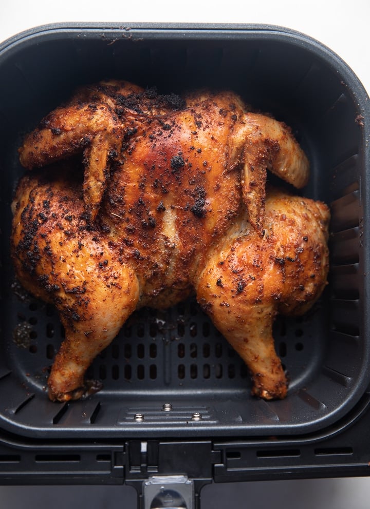 A cooked spatchcok chicken in an air fryer basket