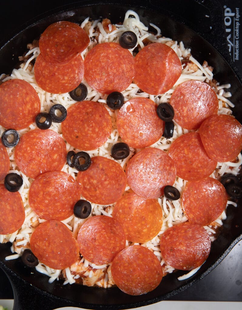 Pepperoni and olives laid on top of the cauliflower.