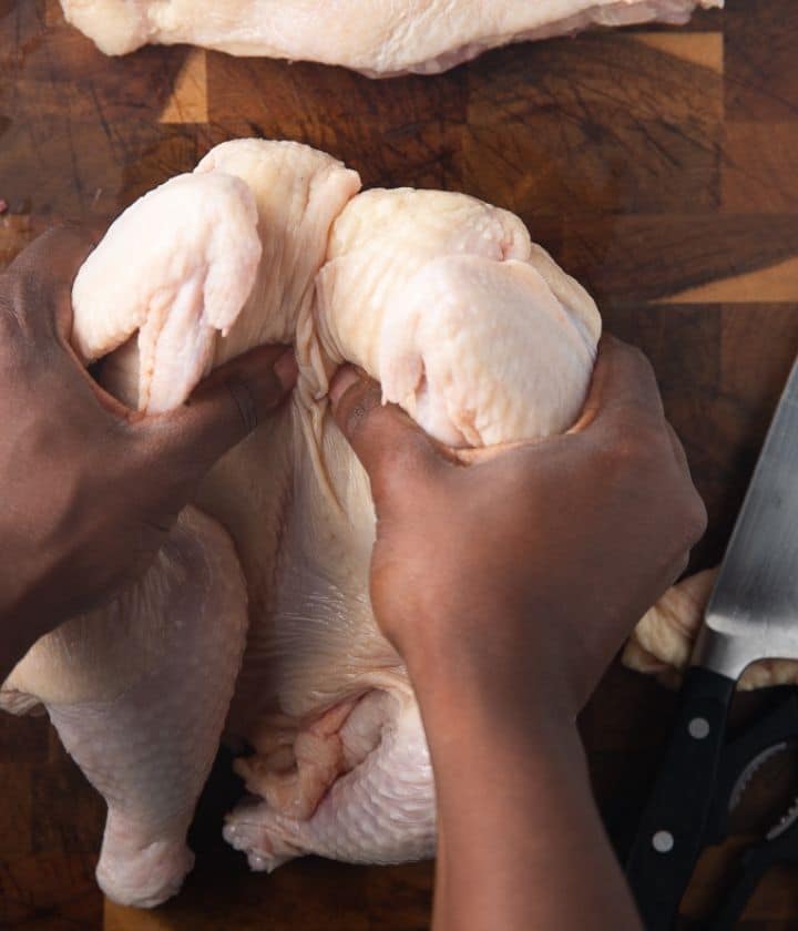 two hands pulling the breast of the chicken apart