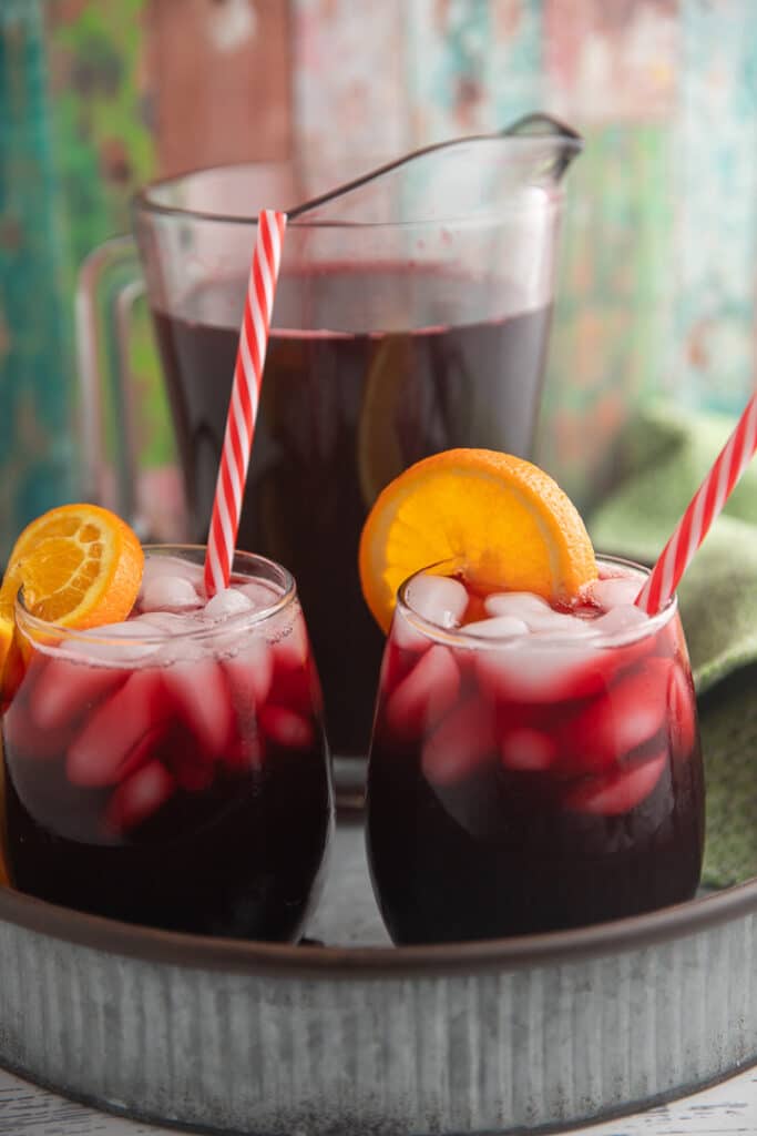 Two glasses of sorrel drink garnished with orange slices